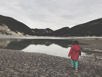 Rear view of girl walking towards lake against cloudy sky