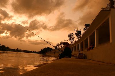 Men fishing at shore against sky during sunset