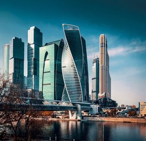 View of modern buildings by river against sky in city