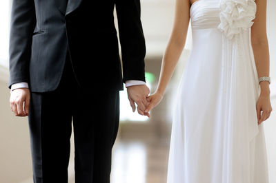 Midsection of bride and groom holding hands during weeding