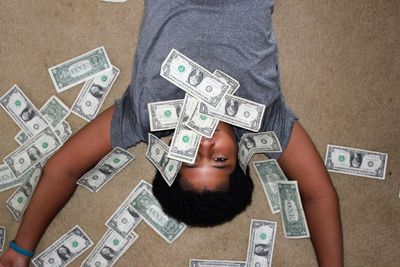 High angle portrait of boy surrounded by money while lying on floor