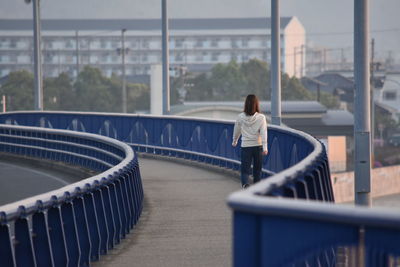 Rear view of woman walking on bridge against building
