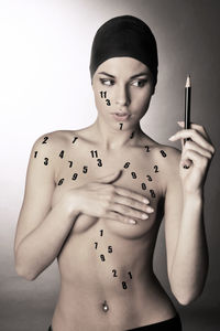 Topless young woman holding pencil against gray background