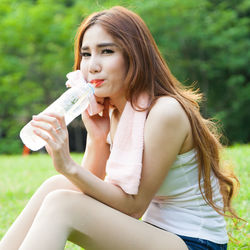 Portrait of woman drinking water from bottle while sitting on field