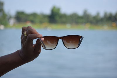 Close-up of hand holding sunglasses against sea