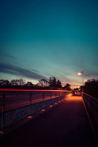 Road by trees against blue sky at sunset