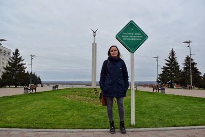 Portrait of woman standing by road sign against monument of glory