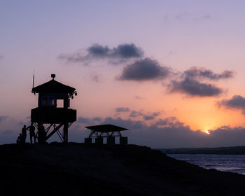 Silhouette hut on beach against sky during sunset