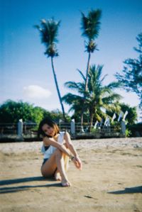 Young woman sitting on sand at beach against sky