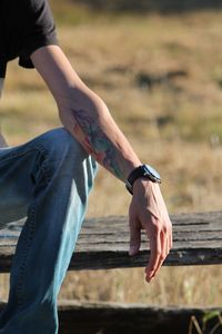 Midsection of young man with tattoo on hand sitting over bench