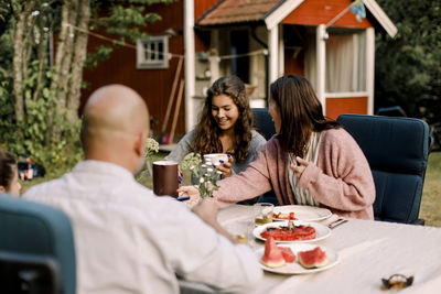 Smiling woman talking to daughter while sitting by dining table in yard