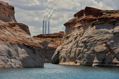 Rock formations at sea shore against smoke stacks