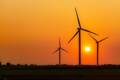 Silhouette wind turbines on field against orange sky