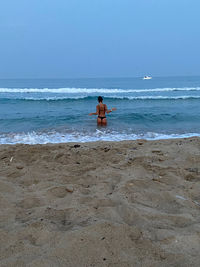 Rear view of shirtless man on beach against sky