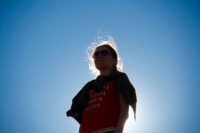 Low angle view of young woman standing against clear blue sky