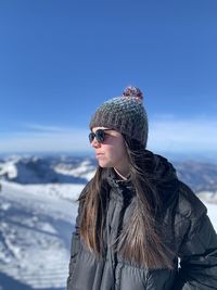 Young woman looking away while standing against sky during winter