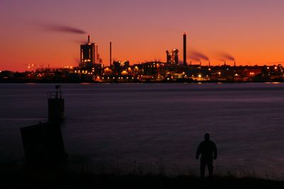 Rear view of silhouette man and illuminated cityscape against sky during sunset