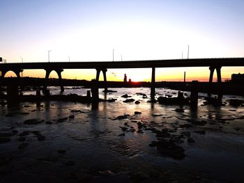 Silhouette bridge over river against clear sky during sunset