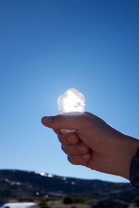 Cropped hand holding ice against clear blue sky