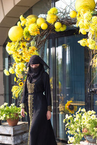 Portrait of young woman standing by flowers