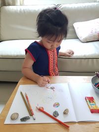 Girl drawing in book on table at home