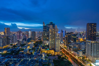 Aerial view of illuminated city buildings against blue sky