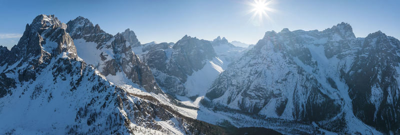 Panoramic view of sun shining over snow covered mountain range during winter