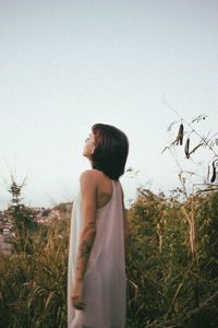 Side view of woman standing on field against clear sky