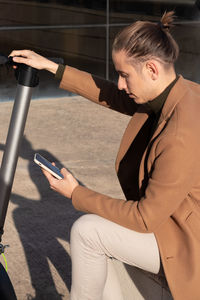 Young man sitting activating the electric scooter app on the smartphone to ride around city center