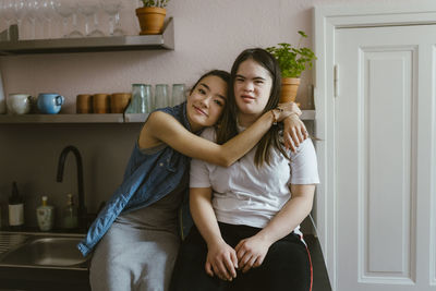 Young woman hugging sister with down syndrome in kitchen at home