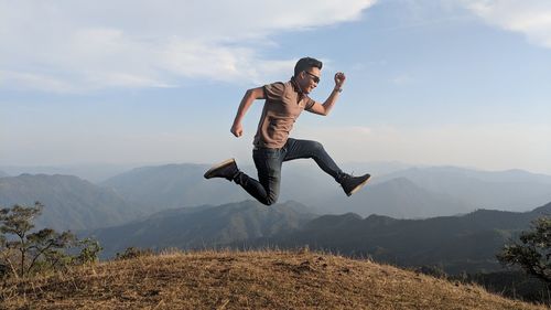 Full length of man jumping in mountains against sky