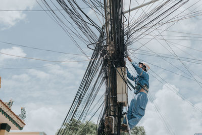 Low angle view of people working on mast against sky