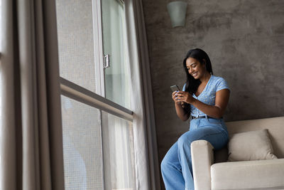 Young black woman working at home with smartphone on her couch in the living room. home office 