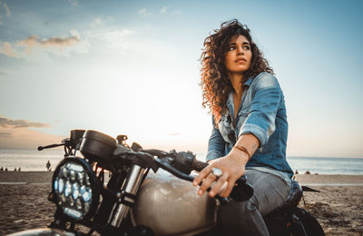 Young woman riding motorcycle on beach against sky