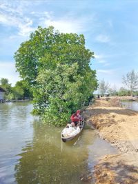 People in boat by river against sky