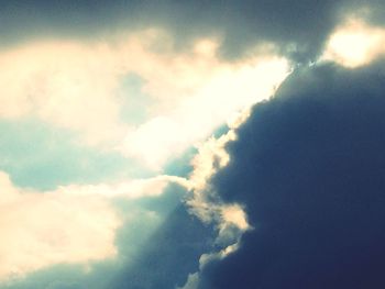 Low angle view of sunbeam in cloudy sky