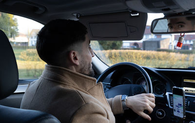 A young oriental man sits behind the wheel of a car.