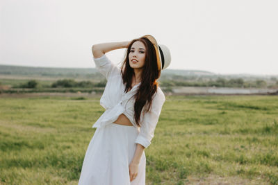 Portrait of smiling beautiful woman wearing sun hat standing on grassy land