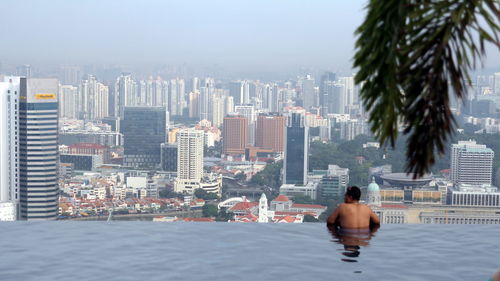 Rear view of shirtless man looking at cityscape while swimming in infinity pool