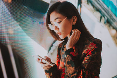 Close-up of young woman using mobile phone standing outdoors at night