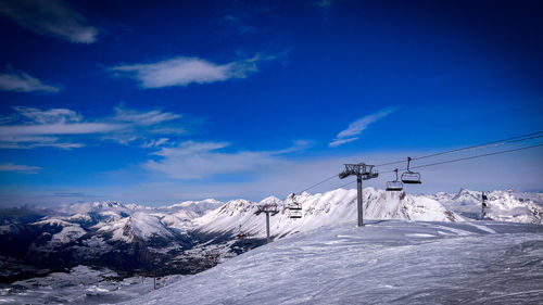 Scenic view of snowcapped mountains and ski lift against blue sky