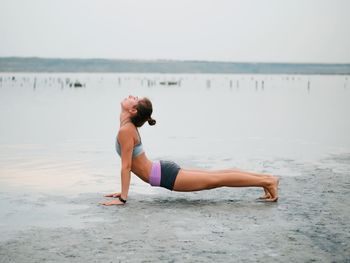 Full length of young woman exercising at beach against sky