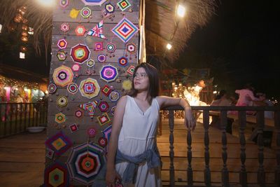 Portrait of woman standing against illuminated railing