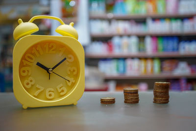 Close-up of yellow clock and coins on table 