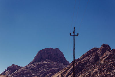 Low angle view of cross on mountain against clear blue sky