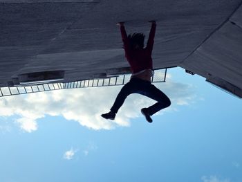 Low angle view of woman jumping against sky