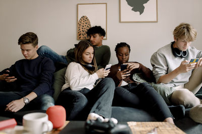 Multi-ethnic friends using social media on mobile phones while sitting on sofa at home