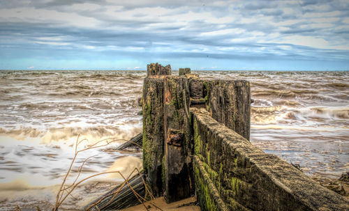 Wooden posts on beach against sky