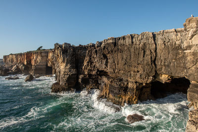 Scenic view of rocks in sea against clear blue sky