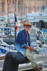 Portrait of senior man sitting on bollard at harbor